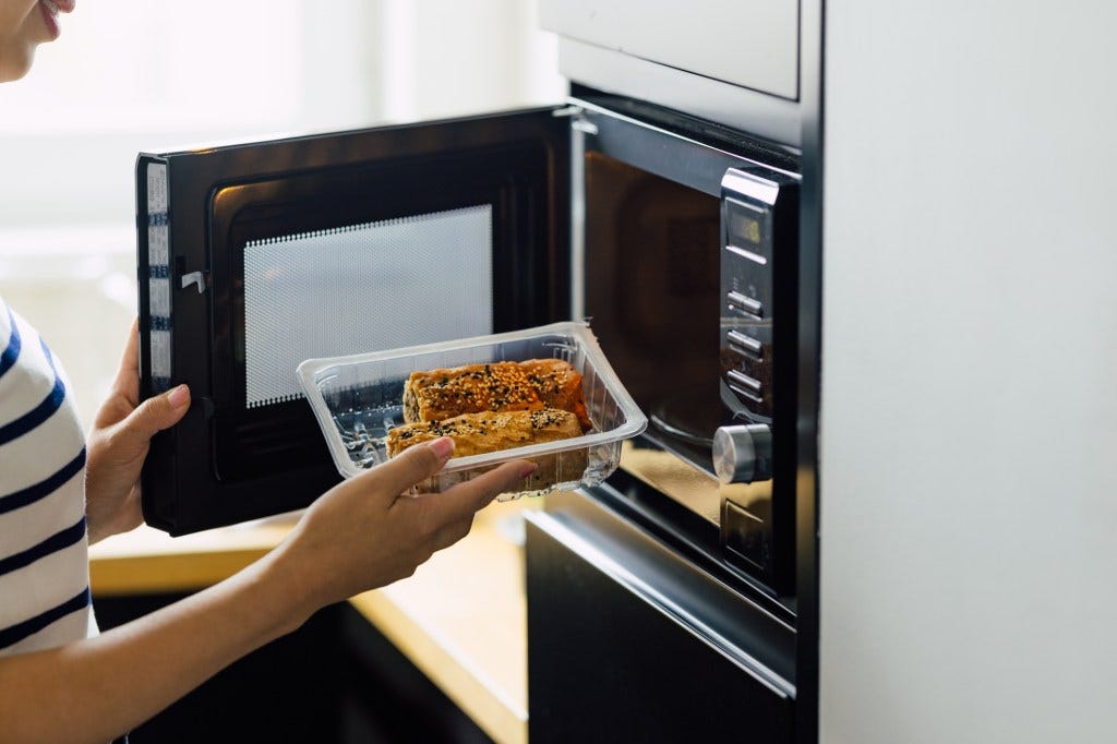 "Stopping the practice of heating food in plastic could be one of the most effective ways to reduce microplastic consumption," the researchers wrote. A woman is shown reheating a meal in a microwave.