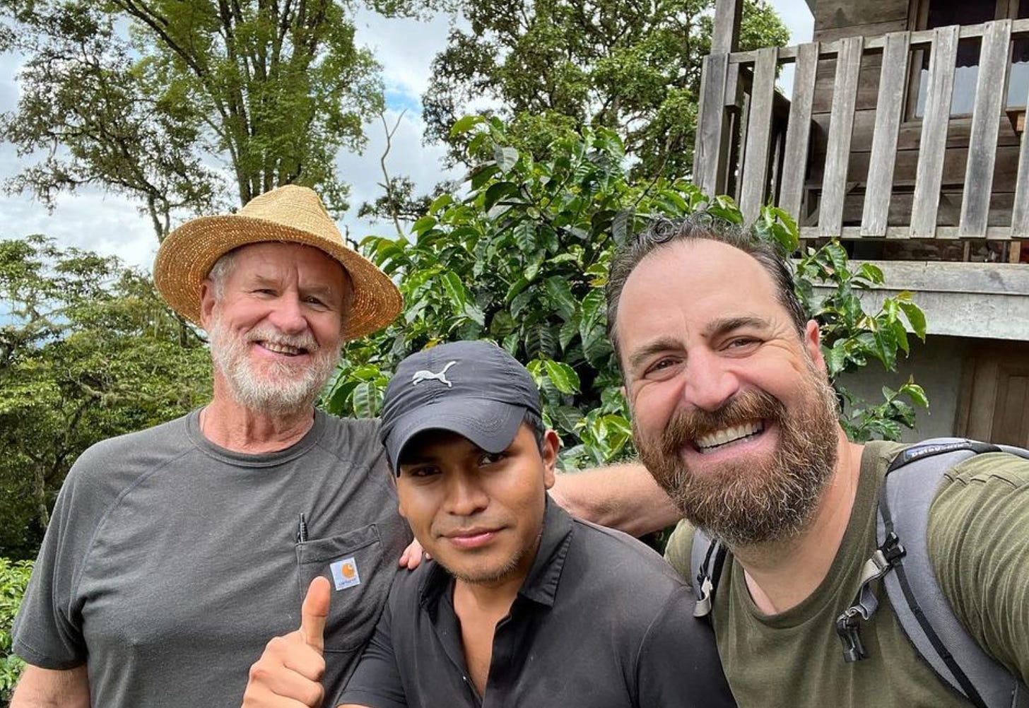 A selfie of three men arm-in-arm on a coffee farm in Latin America.