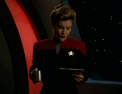 Janeway from Voyager looking at a PADD and indicating WTF