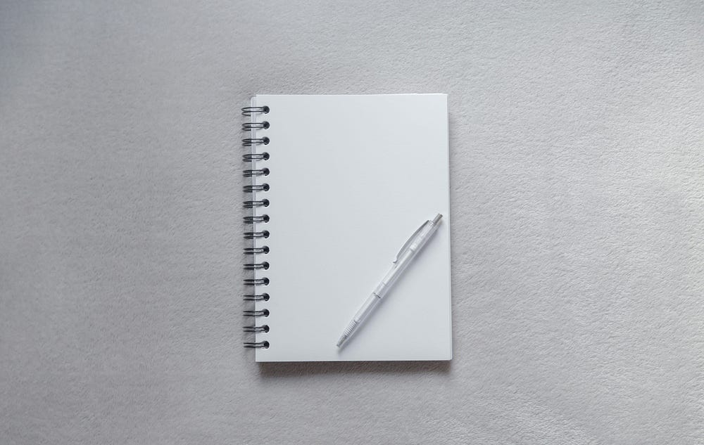 An open notebook with a pen resting on it. The page is blank.