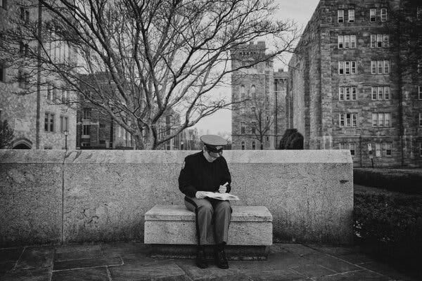 A photograph of a West Point cadet sitting on a bench on campus reading and taking notes.