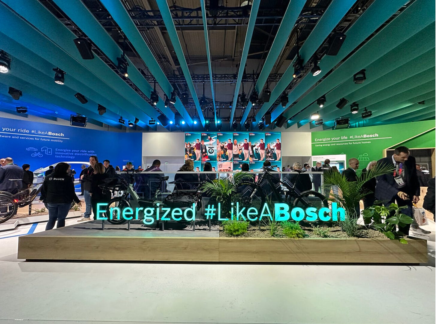 A photo of a convention show floor booth in blue and green colors, decorated with plants, and text that reads Energized Like A Bosch.
