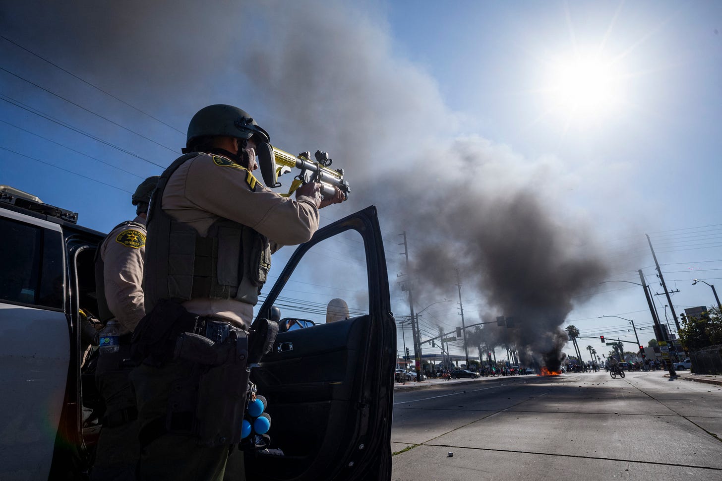 A law enforcement officer aims his firearm close to the site of a burning vehicle in the Compton neighborhood of Los Angeles A law enforcement officer aims his firearm close to the site of a burning vehicle in the Compton neighborhood of Los Angeles