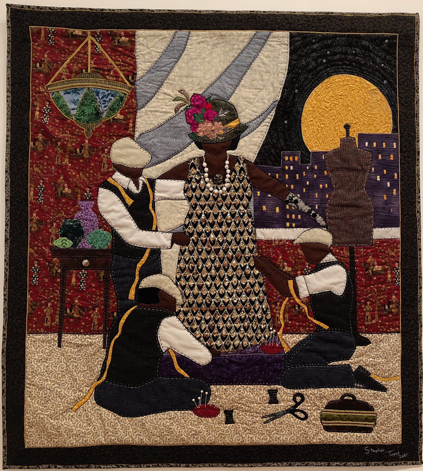 Quilt showing an African American woman at a dress fitting, attended by three African American men. The room contains a side-table and hanging lampshade. Skyscrapers and a yellow moon are visible through a large window.