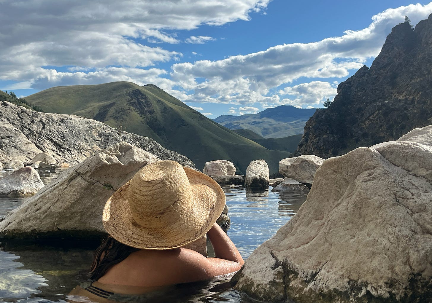 Person wearing sunhat soaking in hot spring looking in canyon.