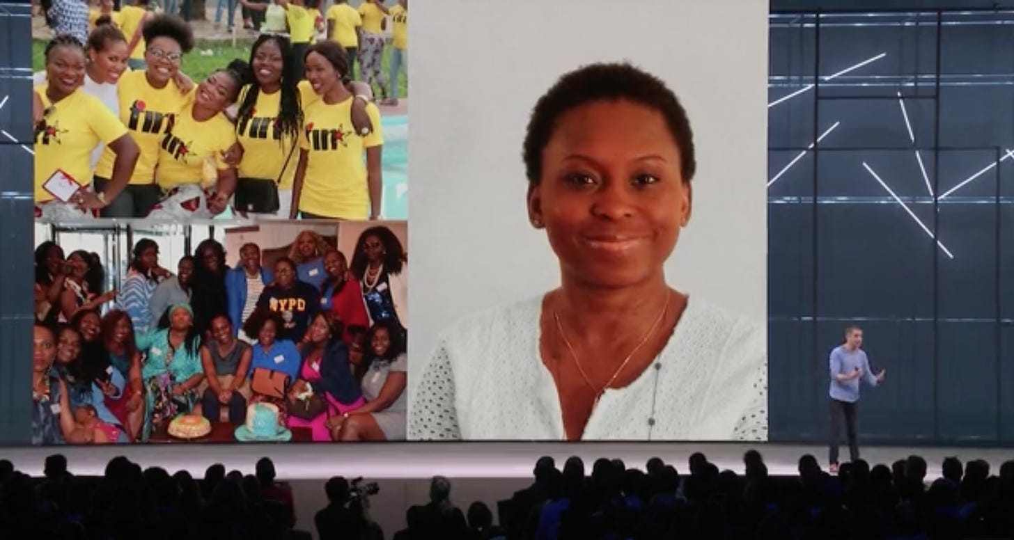 A screenshot of a video with a white man in a blue shirt on stage in front of a large crowd, with a huge video screen behind him. On the right of the screen is a photo of Lola, an African woman with close cropped hair and a white shirt. On the left are two group photos of Black women gathering together in real-life FIN meet-ups.