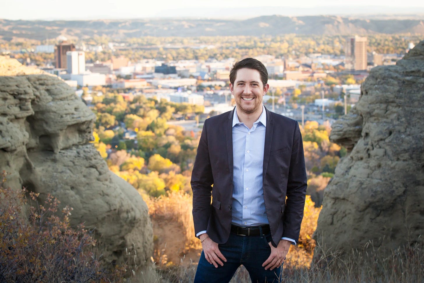 smiling man in suit between rocks overlooking city