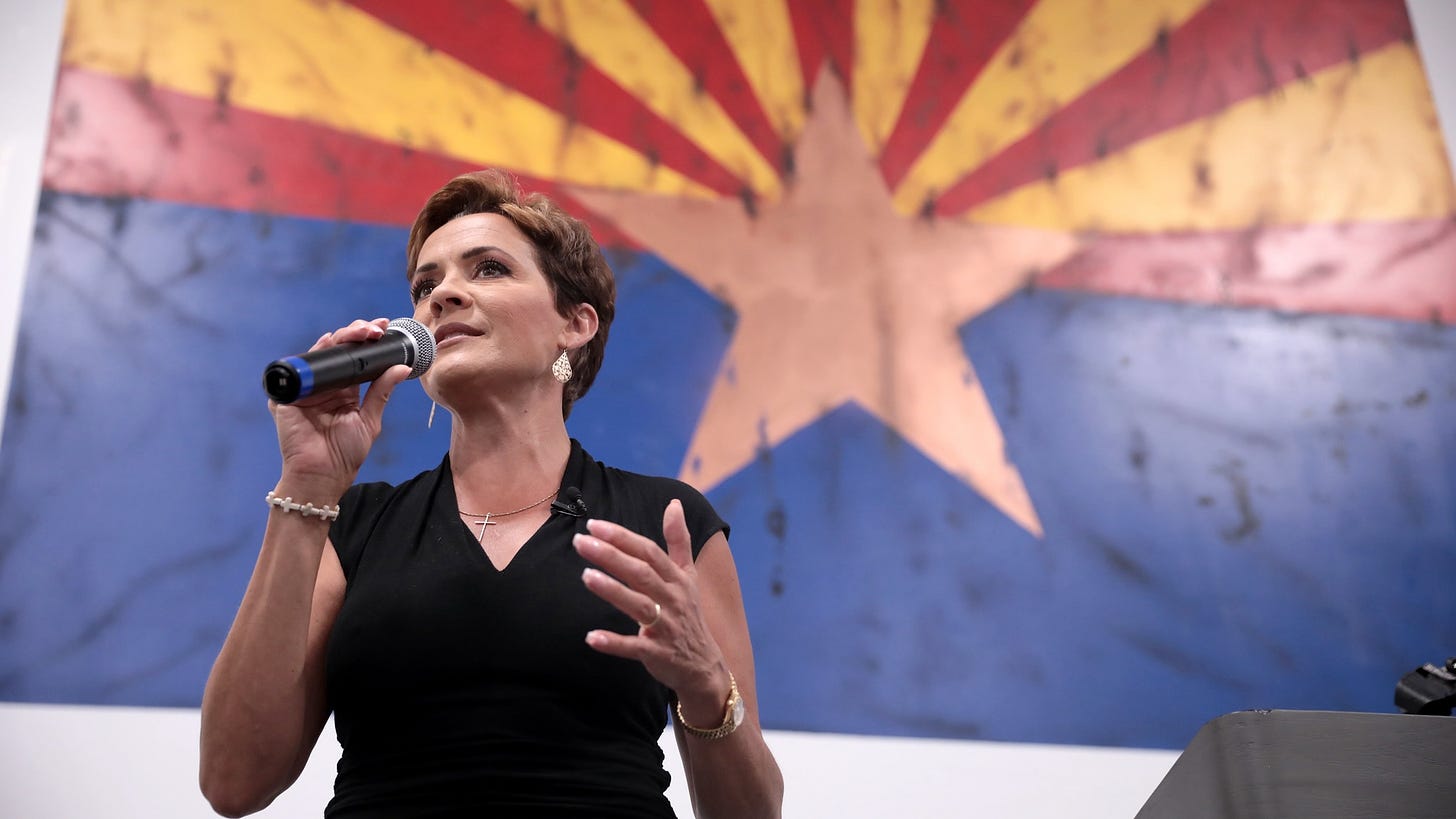 Republican candidate for Senate Kari Lake holds a microphone in front of the Arizona flag.