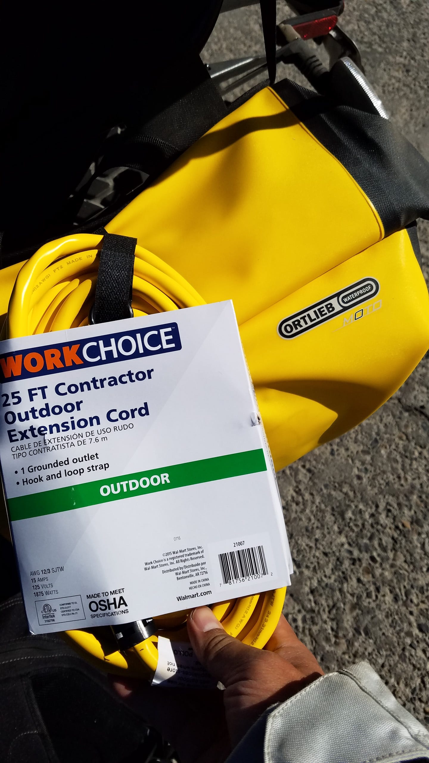 A 25ft yellow extension cord, just purchased and still bound by it's paper sleeve, sits on top a yellow saddlebag. A label on the saddlebag says, "Ortlieb waterproof"