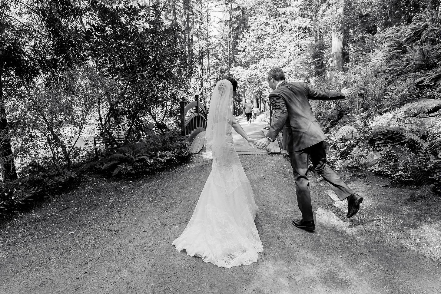 Evelyn and Tom dance-skipping away after their wedding ceremony; Evelyn in long white lace gown; Tom in gray suit; forest setting