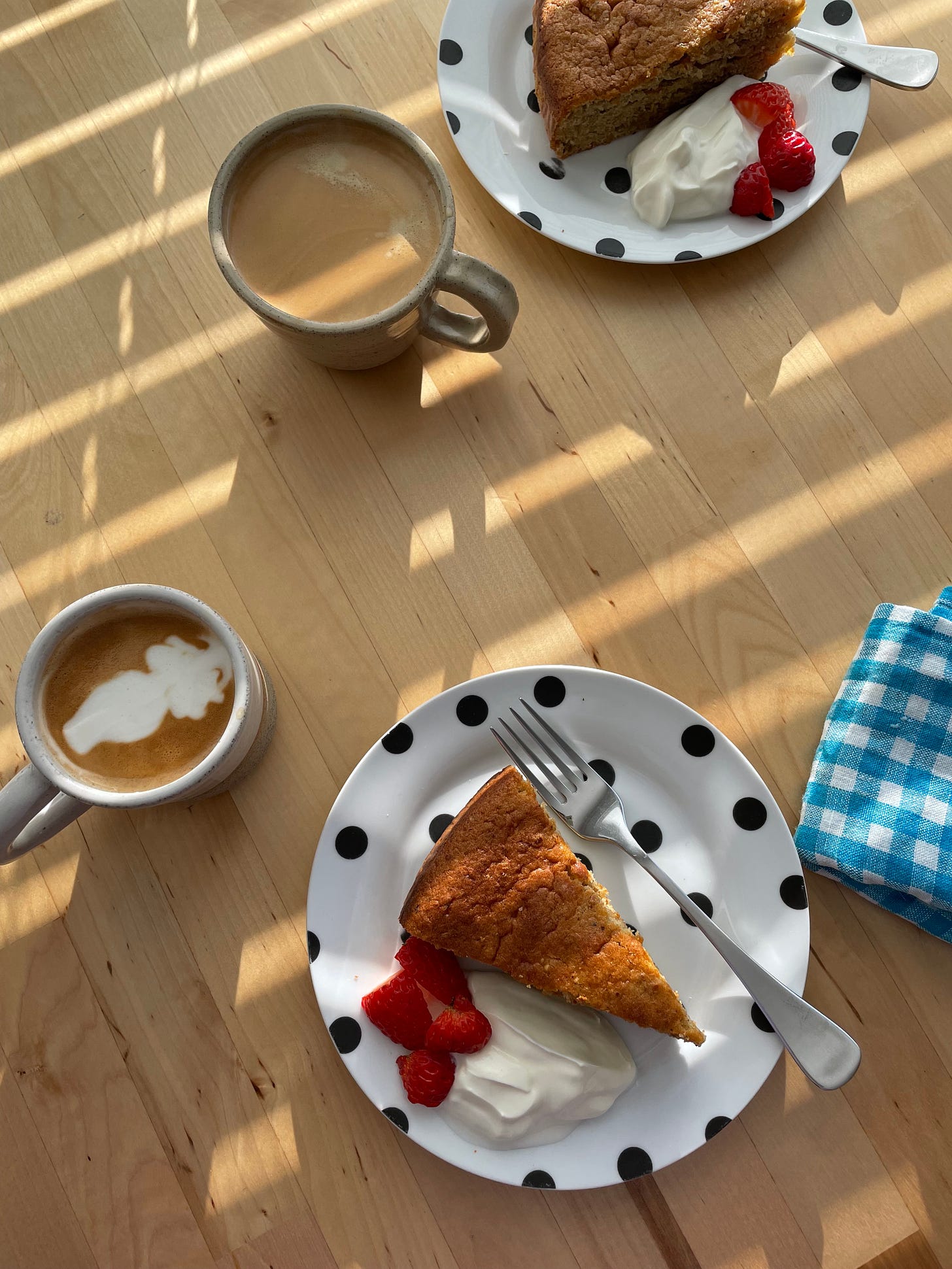 Slices of hazelnut cake with yoghurt and strawberries sitting on a breakfast table with cups of coffee