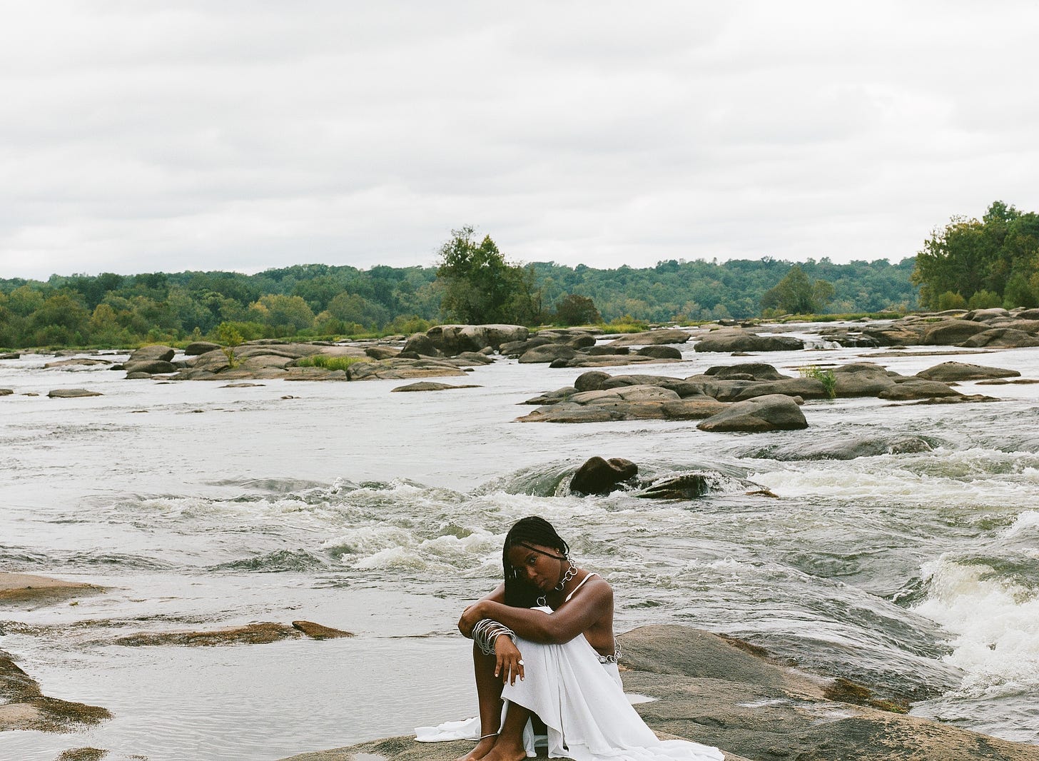 Sitting on river rocks in a white dress made with my needle and need as eager water gushes behind me. The distant horizon is lined with green trees and the sky is made of cotton.