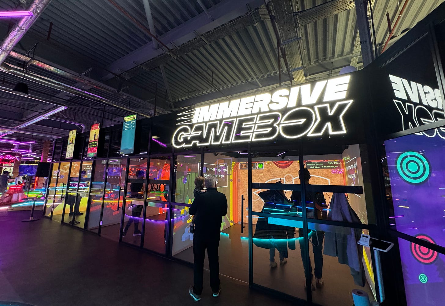 A row of Gamebox rooms; we can see through their rear glass walls into the people playing them inside
