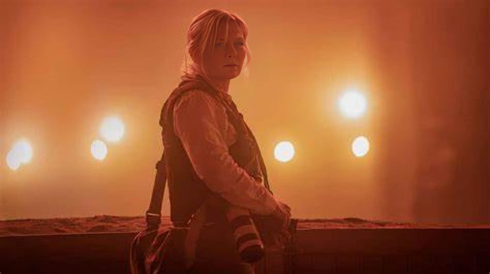 A press reporter stands against a hazy, dusty backdrop illuminated by eerie orange lights, capturing the tension and uncertainty in the film's atmosphere.
