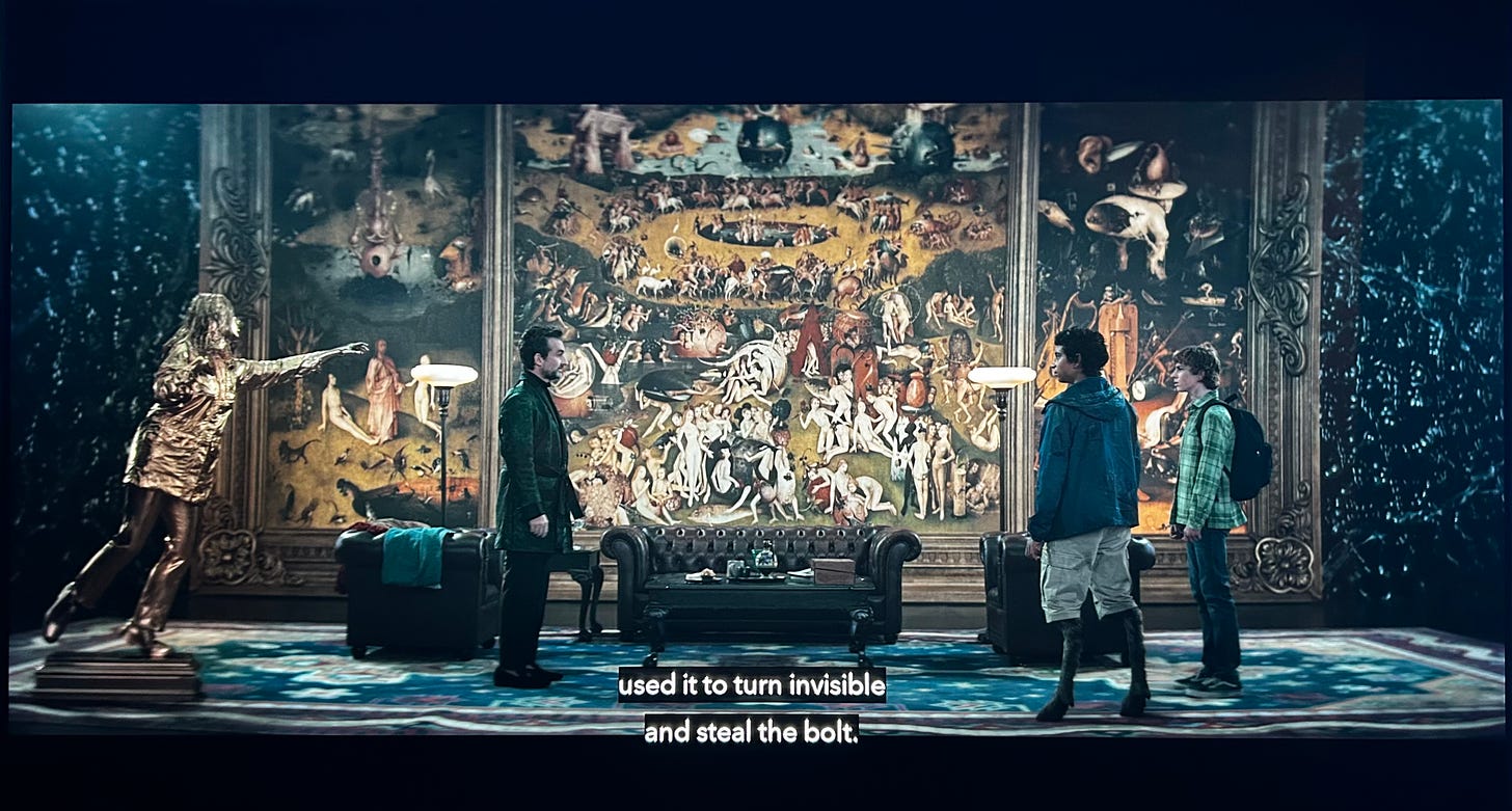 Widescreen shot of Hades, Grover, Percy, and Sally (in gold) in a living  room set up. The backdrop is Bosch's Garden of Earthly Delights