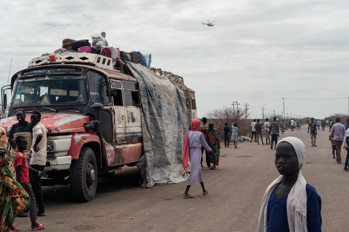 A UN helicpopter flys over head as aold bus is loaded on the main road through Renk.