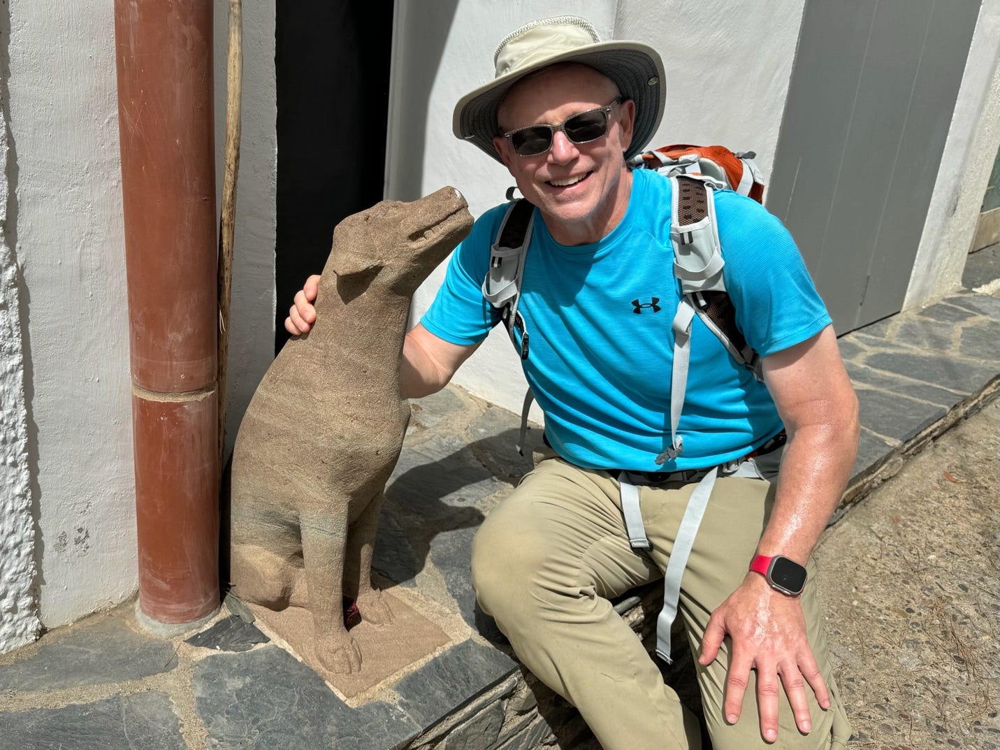 A person sitting on a stone ledge with a statue of a dog

Description automatically generated