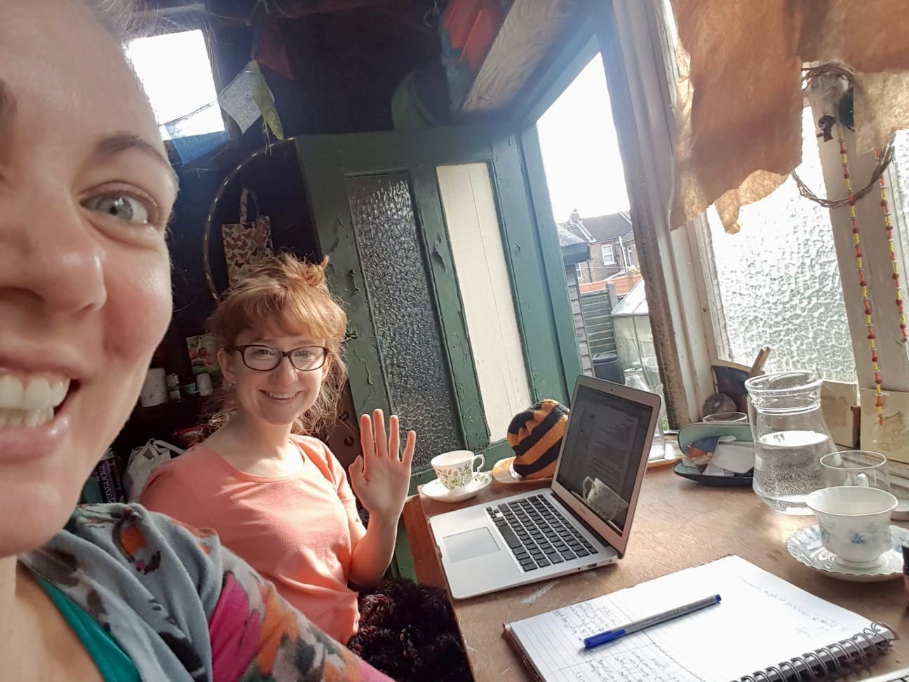 two women in a shed one with a laptop one with a notebook smiling to the camera