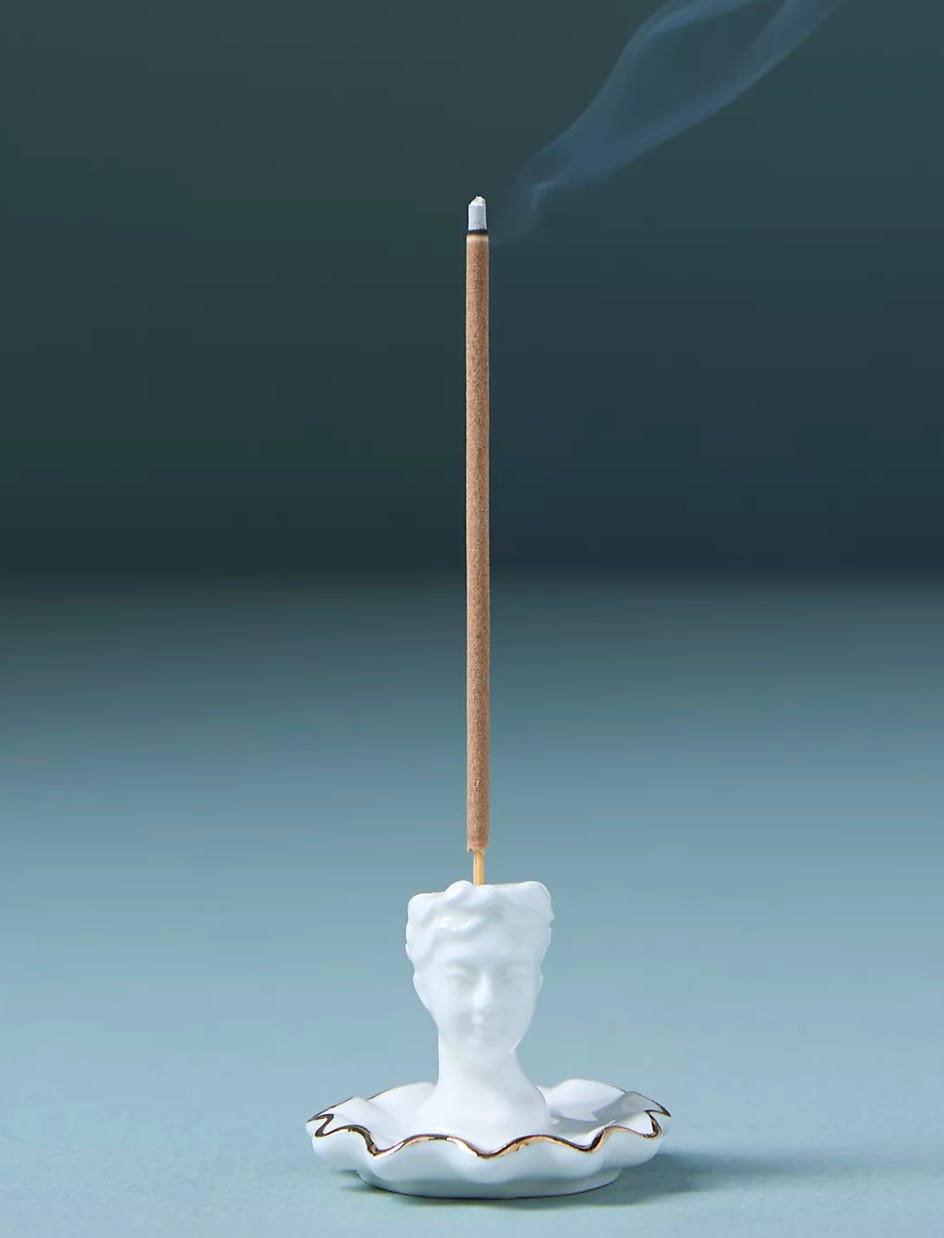 One stick of incense sits in a holder that looks like a white ancient bust