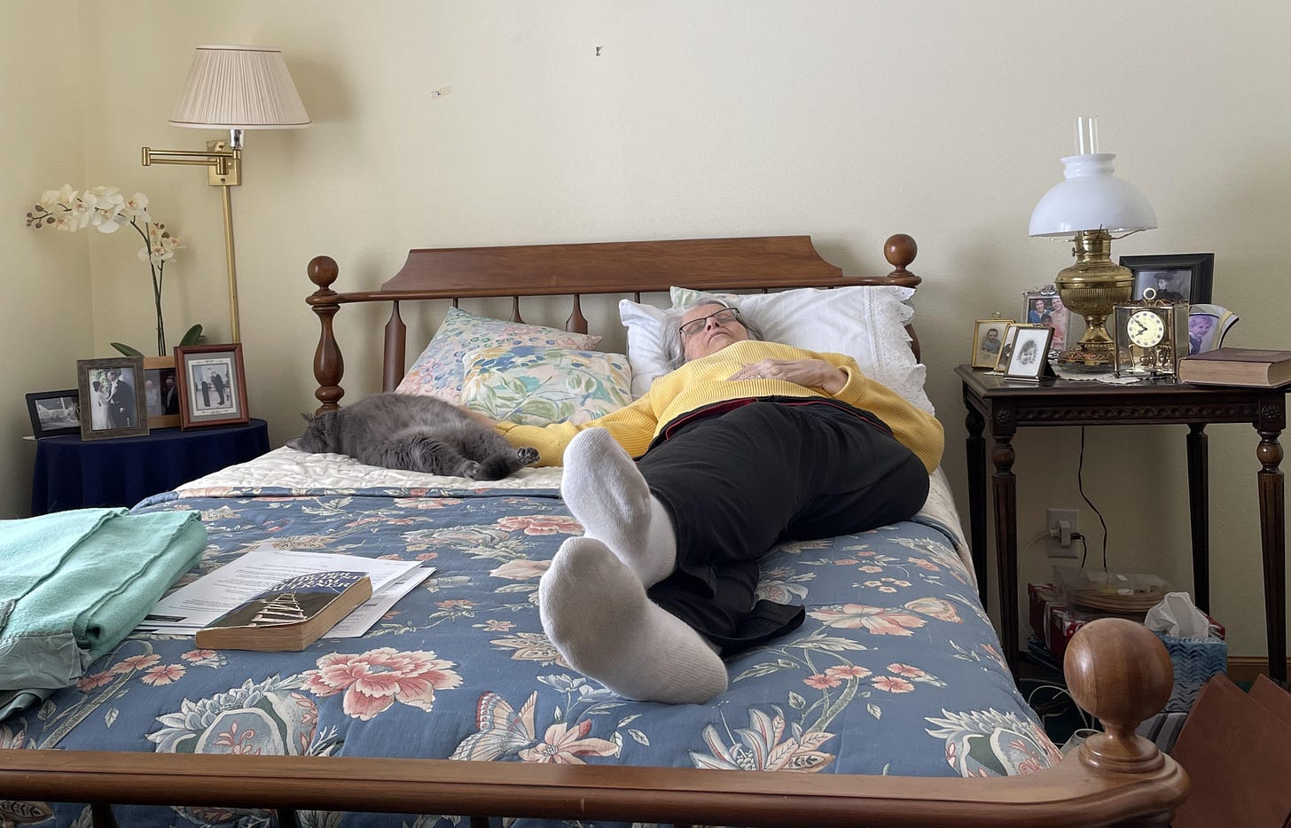 A sleeping senior woman lies on a bed with a sleeping senior catwith 