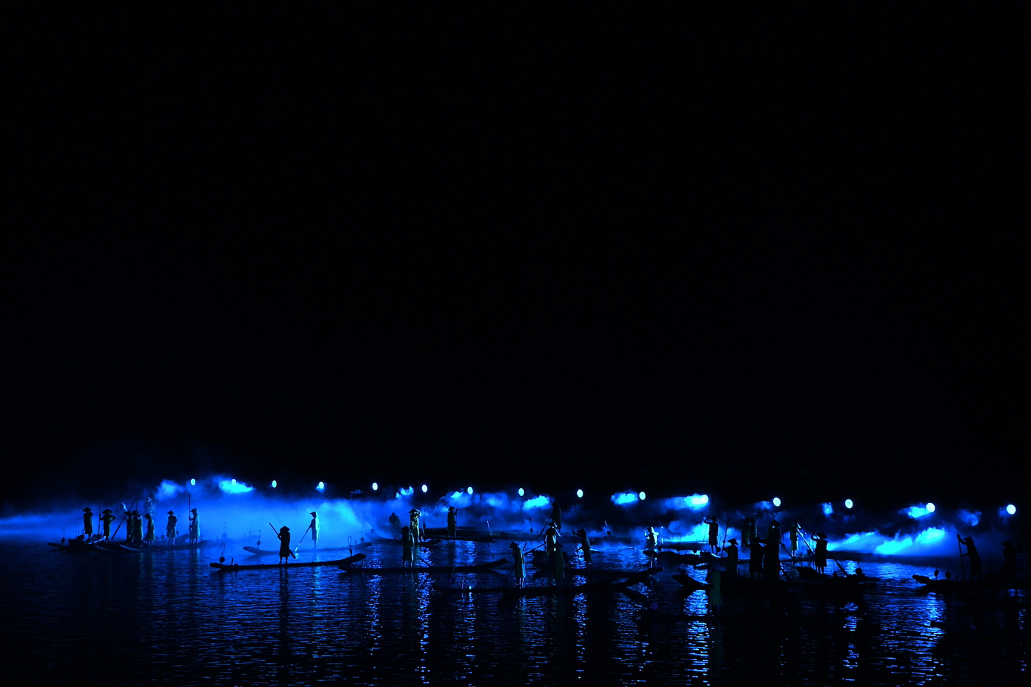 Il cielo della notte è nero; sul fiume, uomini in barca sono illuminati da luci azzurrognole.