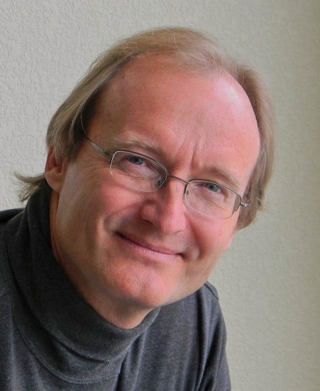 Headshot of a smiling man with slightly receding hairline wearing glasses