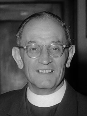 Black and white photograph of Martin Niemöller. He is a white middle-aged man wearing clerical clothing and glasses.