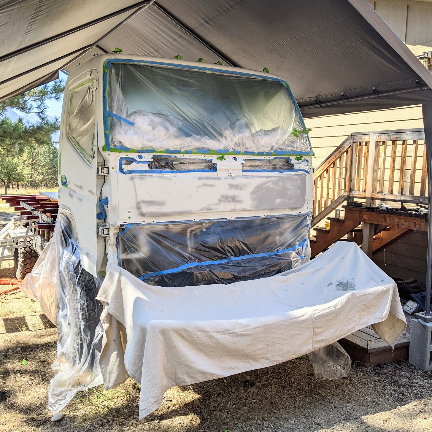 white work truck, covered with plastic sheeting and blue and green painter's tape to cover windows and other parts that shouldn't be painted