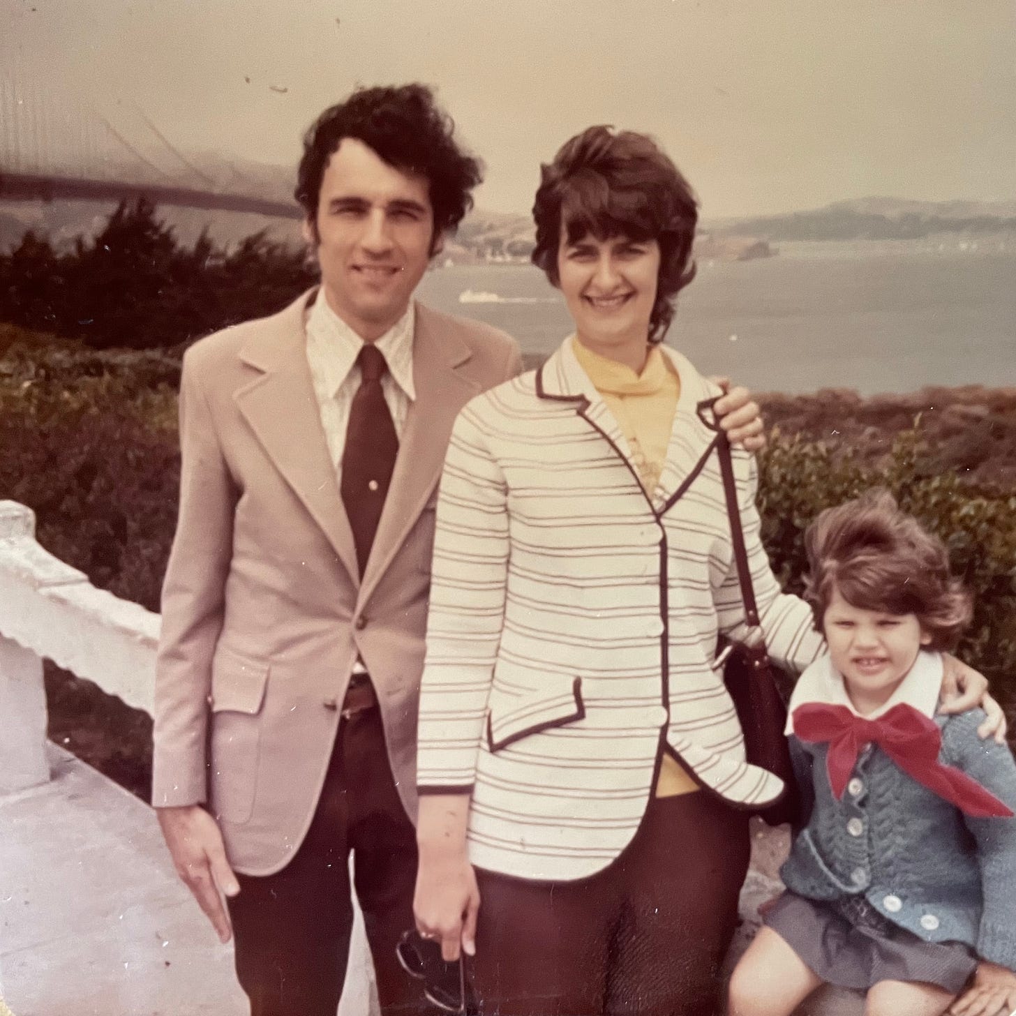 A dressed-up man, woman and girl smile in front of a fog-engulfed Golden Gate Bridge in the early 1970s