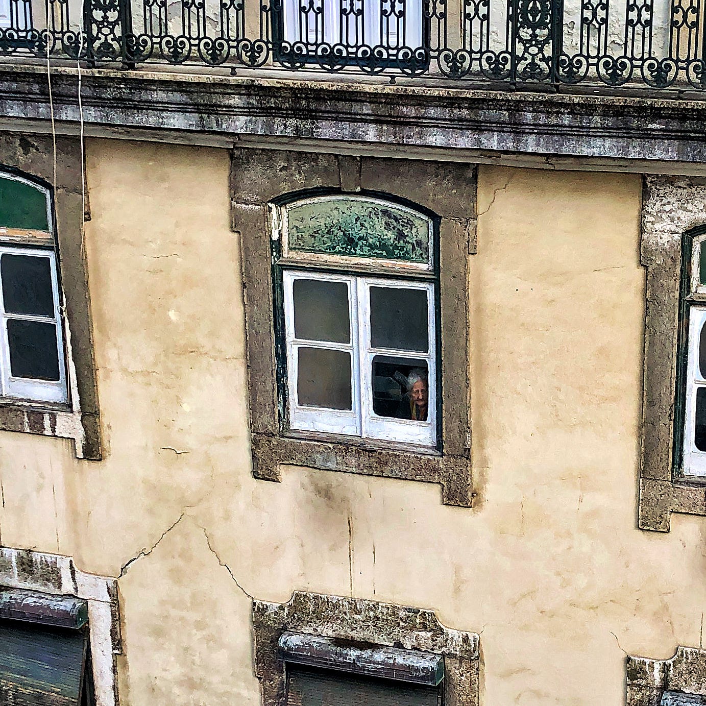 Elderly lady peeking out of a window in the Chiado district of Lisbon, Portugal.