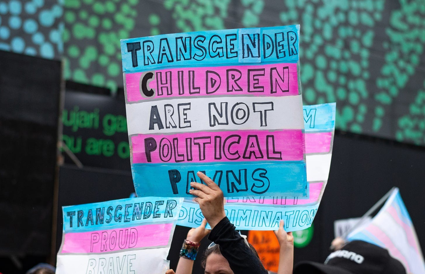 Pink white and blue sign reads "Transgender children are not political pawns" in trans rally