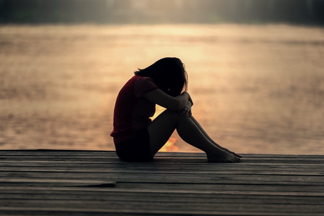 Free A woman sitting alone on a wooden dock by the lake, showing solitude and reflection. Stock Photo