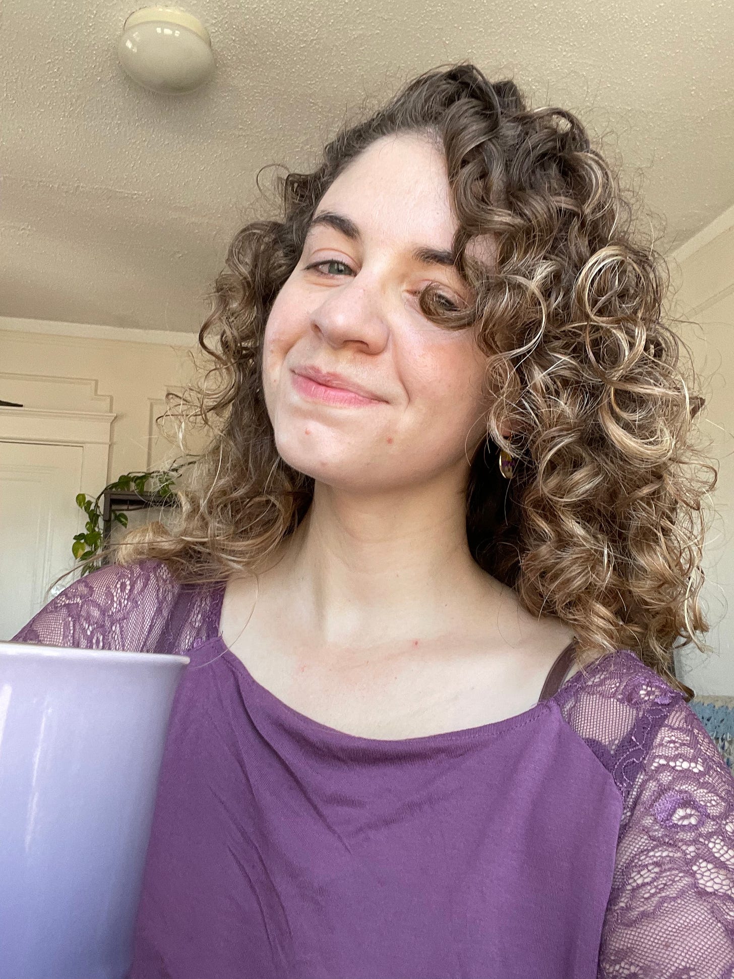 A blonde woman with curly hair in a purple shirt holding a purple mug