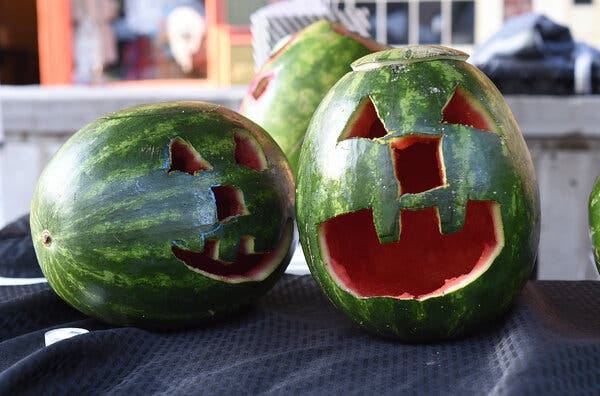 A photo of two watermelons that have been carved into jack-o’-lanterns.