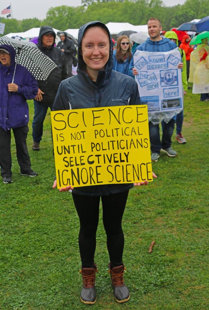 A woman at a protest in the rain, holding a sign that says, "Science is not political until politicians selectively ignore science."