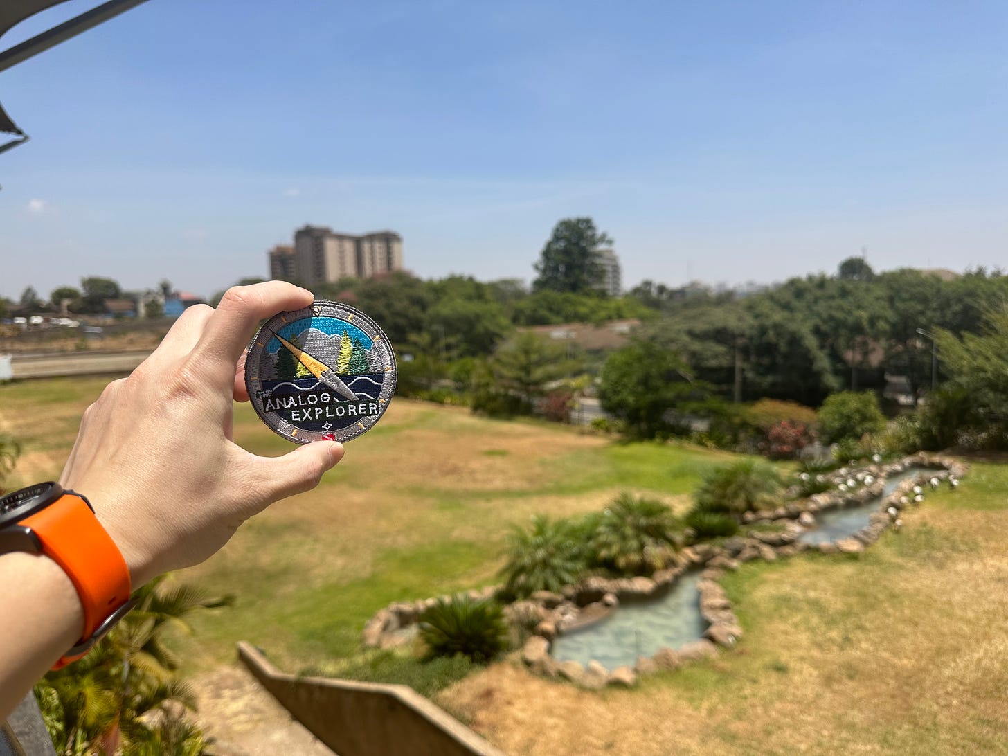 ANalog Explorer patch being held up to the skyline of Nairobi 