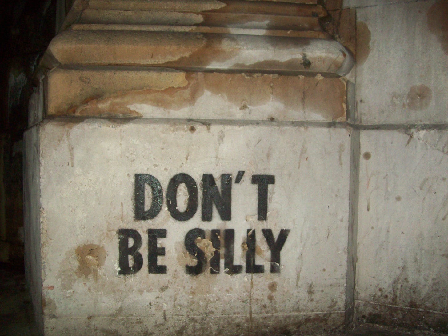 A stenciled graffito on a stone wall: it says "don't be silly."