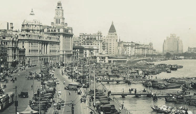 Office buildings, cars, trams on The Bund, the waterfont area in the Shanghai International Settlement early in the 20th Century. Moored at the quays many boats