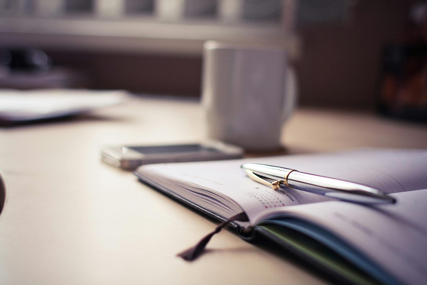 Cup of coffee, smart phone, day planner, and a pen.