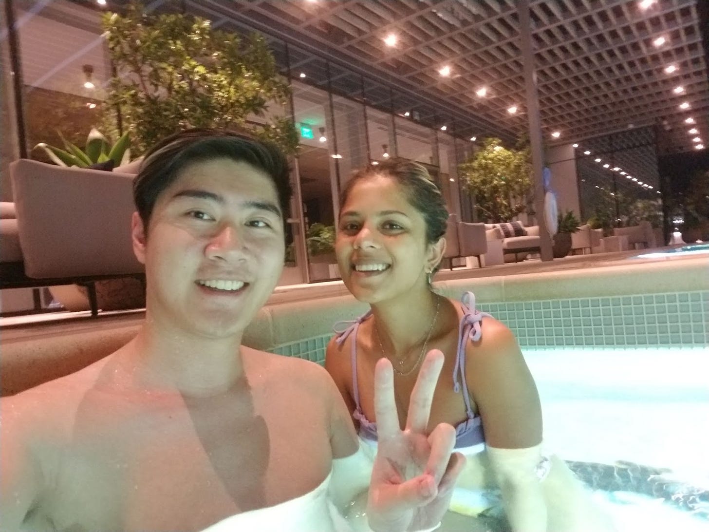 Anthony and his friend smile in a hot tub. Anthony throws up a peace sign.