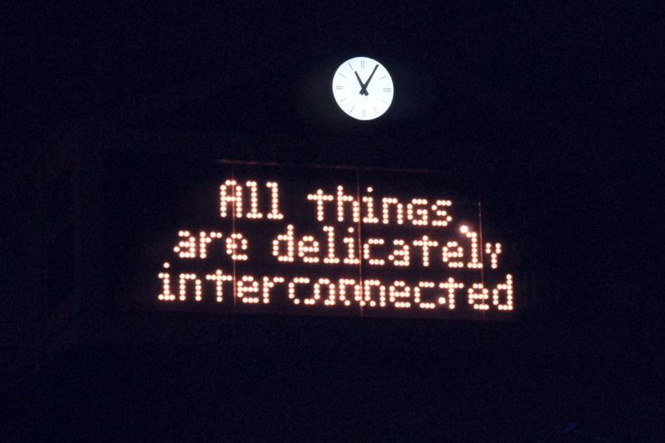 This may contain: an illuminated sign that says all things are delistral interconnected with a clock in the background