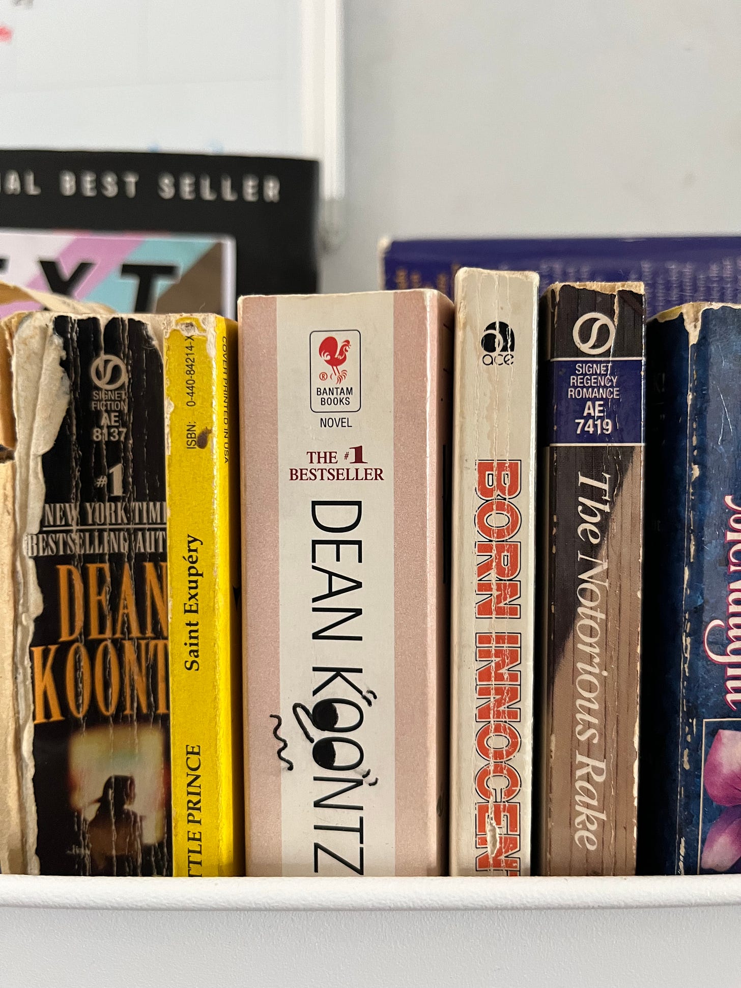 Photo of some of my books lined up on a book cart, including a book by Dean Koontz where I doodled little eyeballs in the two O's and gave it a funny nose and mouth.