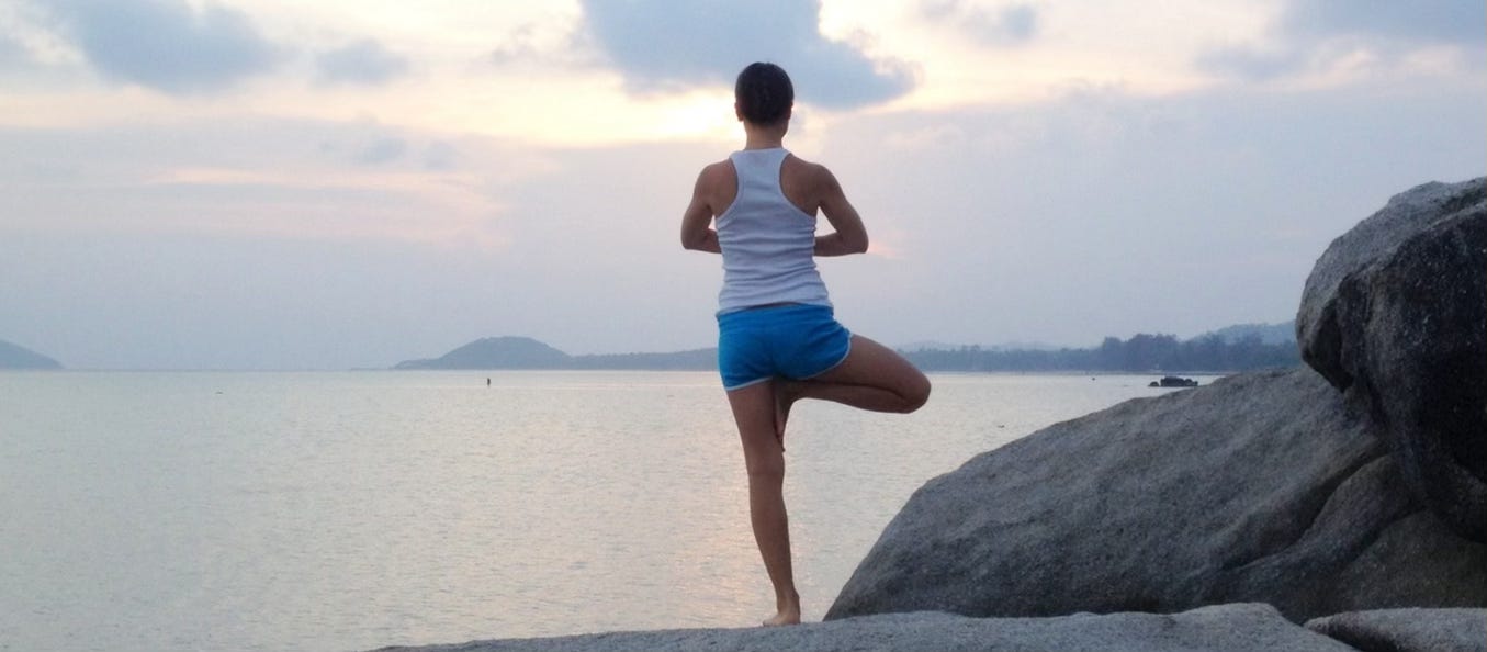 A person standing on rocks in a yoga pose, facing a lake