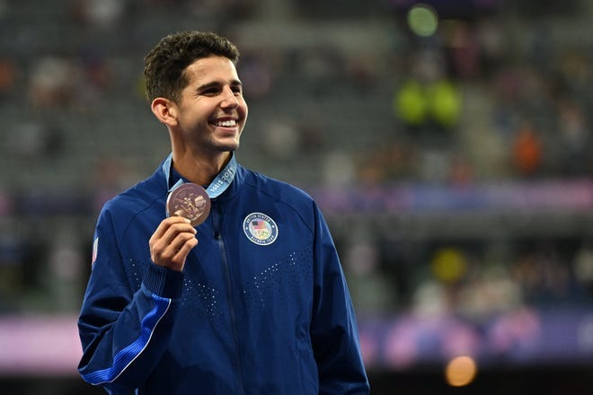 Bronze medallist US' Grant Fisher celebrates on the podium after competing in the men's 5000m final of the athletics event during the Paris 2024 Olympic Games at Stade de France in Saint-Denis, north of Paris, on August 10, 2024. (Photo by MARTIN BERNETTI / AFP) (Photo by MARTIN BERNETTI/AFP via Getty Images)