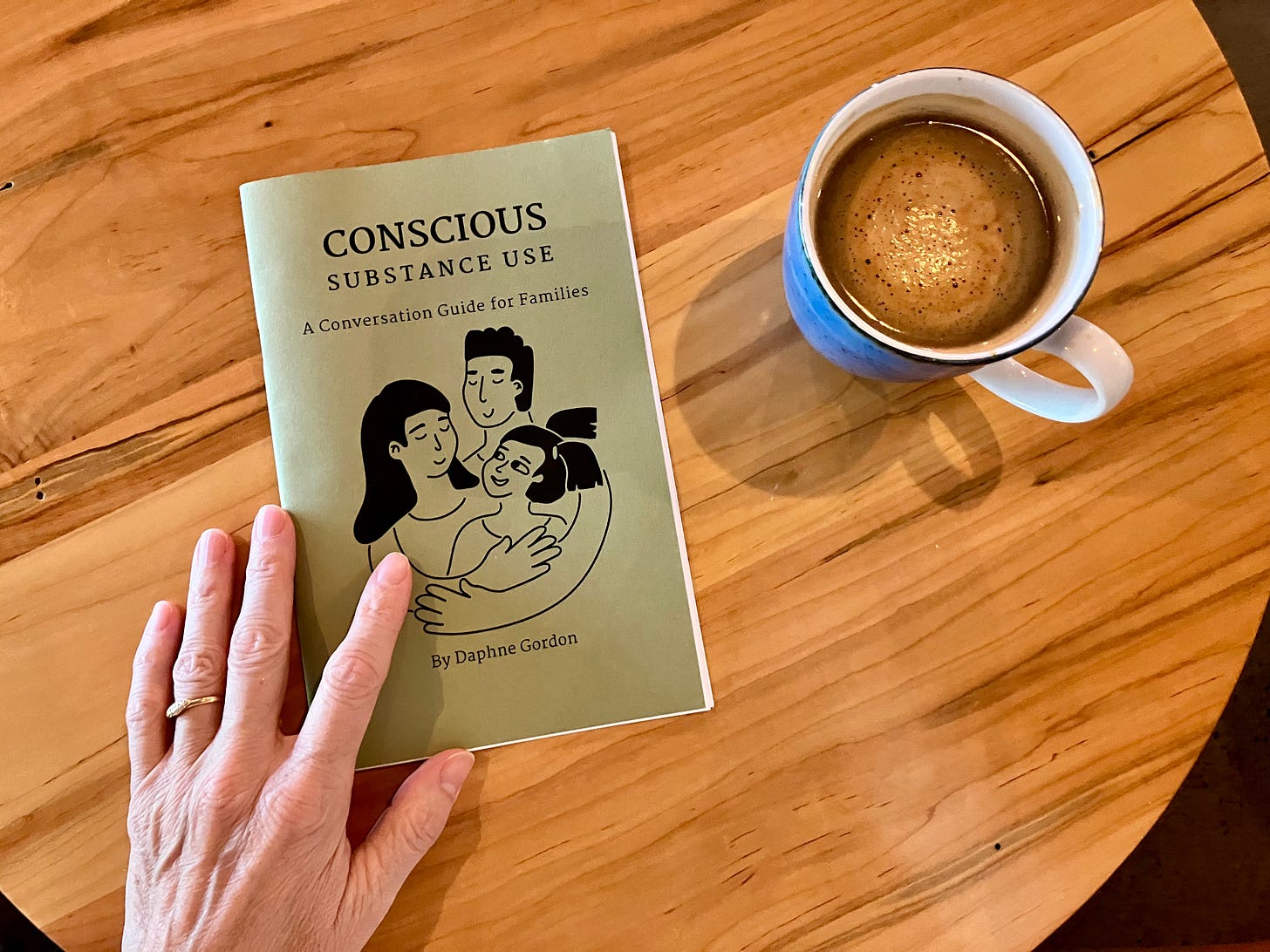 A photograph shows a zine resting on a table. A woman's hand rests on top of the zine. A coffee sits nearby.