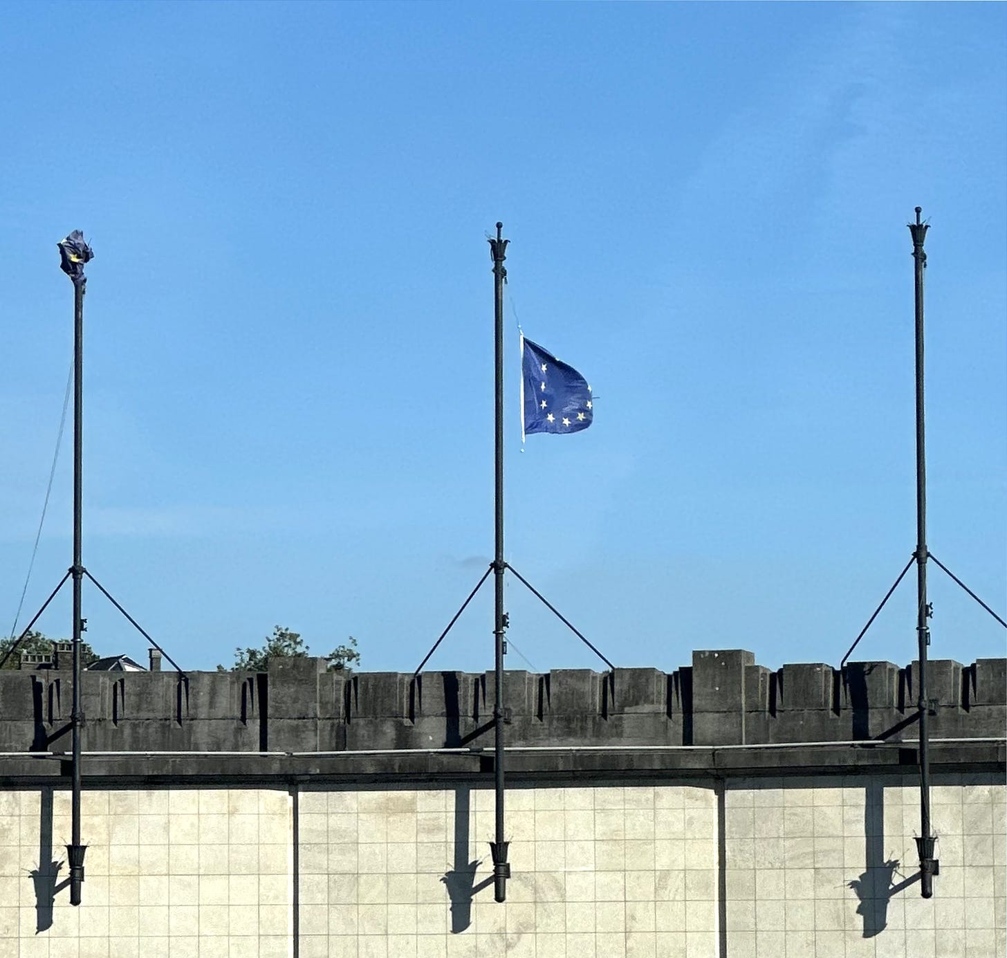An EU flag flies atop a building with two other flagpoles beside it.