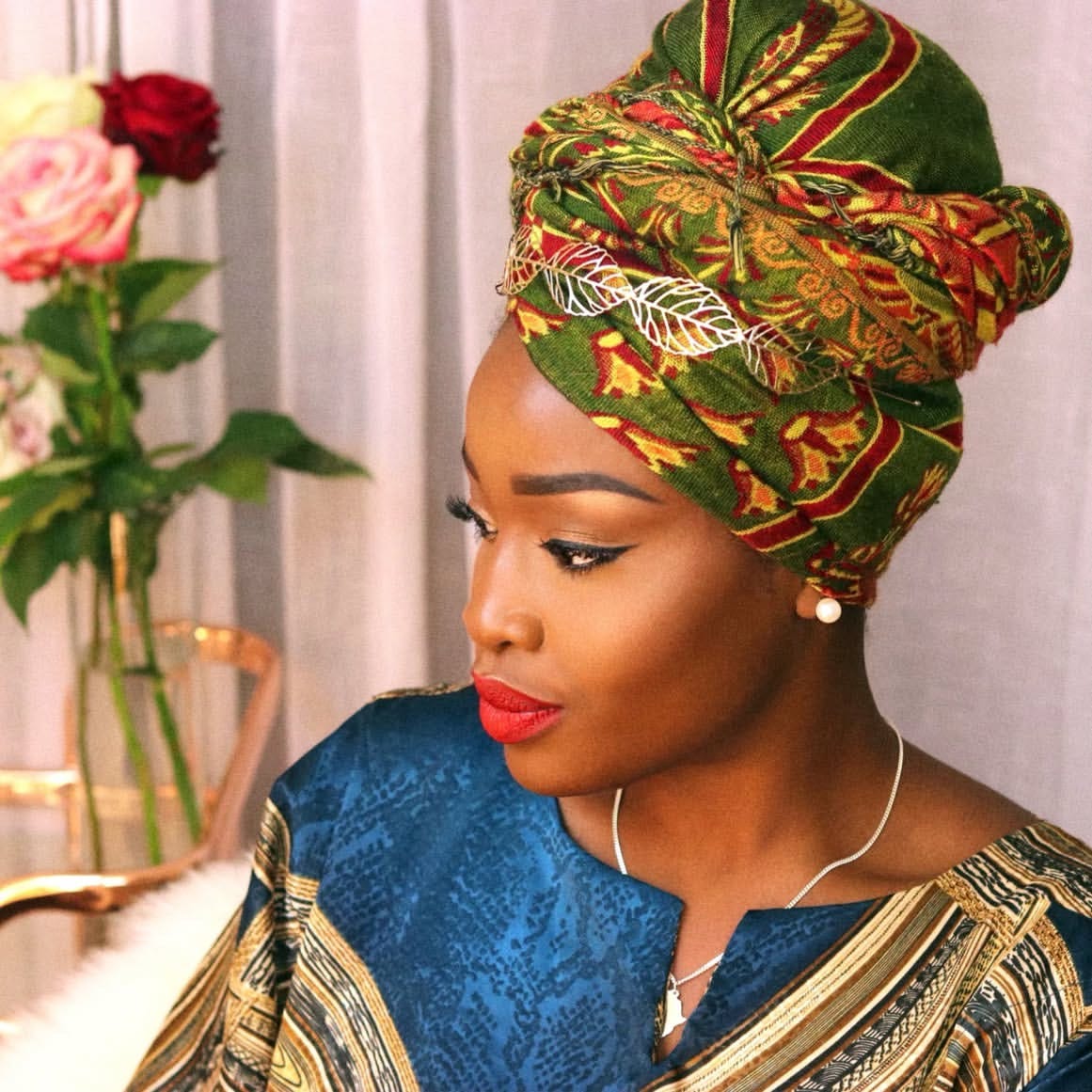 Side profile of Lovette Jallow, Black neurodivergent writer and justice strategist, in a green and red headwrap with gold leaf detail. Photographed in soft lighting beside roses, she looks away thoughtfully. Side profile of Lovette Jallow, Black neurodivergent writer and justice strategist, in a green and red headwrap with gold leaf detail. Photographed in soft lighting beside roses, she looks away thoughtfully.