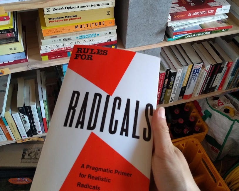 Hand holding the book 'Rules for Radicals' in front of bookshelves