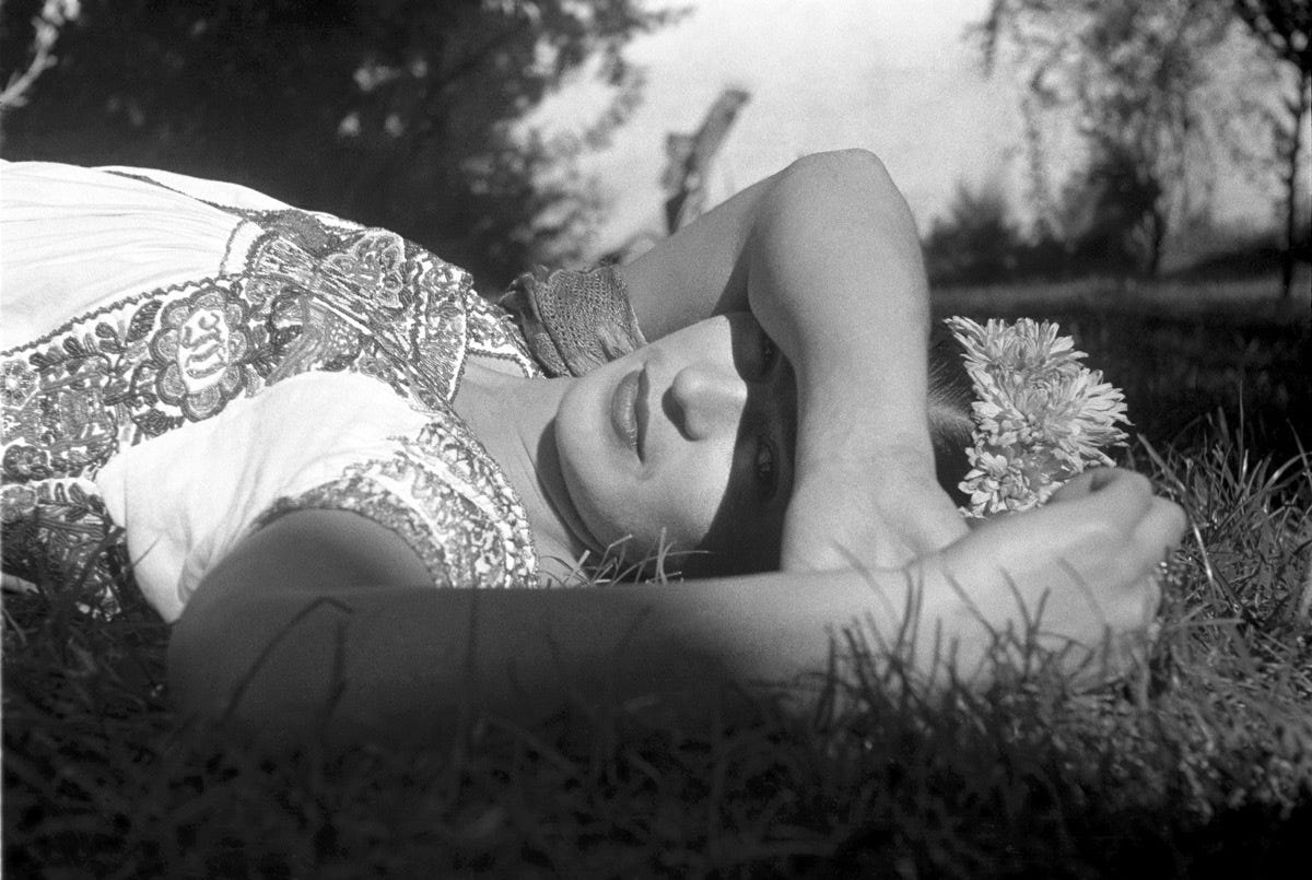 A woman lying on grass with one arm over her eyes.