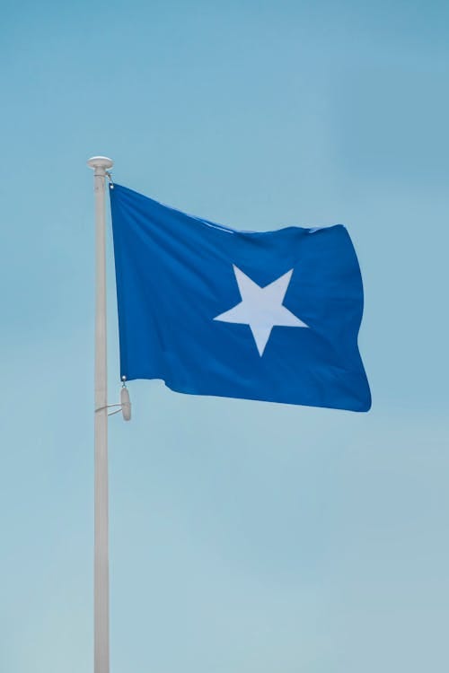 Free The national flag of Somalia waving proudly on a flagpole against a clear blue sky. Stock Photo